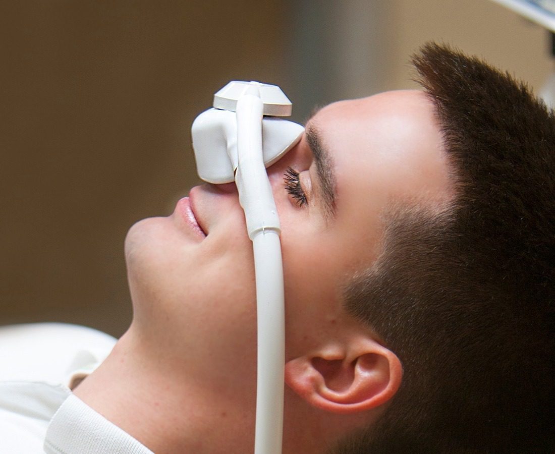 A person lying down with a nasal mask on their face, likely receiving nitrous oxide or oxygen, typically used for sedation or relaxation during a medical or dental procedure.