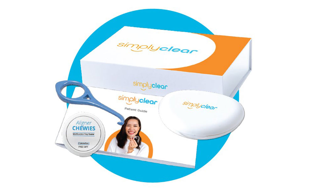 A SimplyClear aligner kit displayed on a blue circle background, featuring a branded box, aligner case, aligner chewie container with a smiling woman’s photo, an aligner removal tool, and a patient guide booklet.
